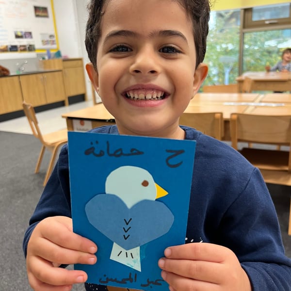 Child smiling holding bird artwork in classroom